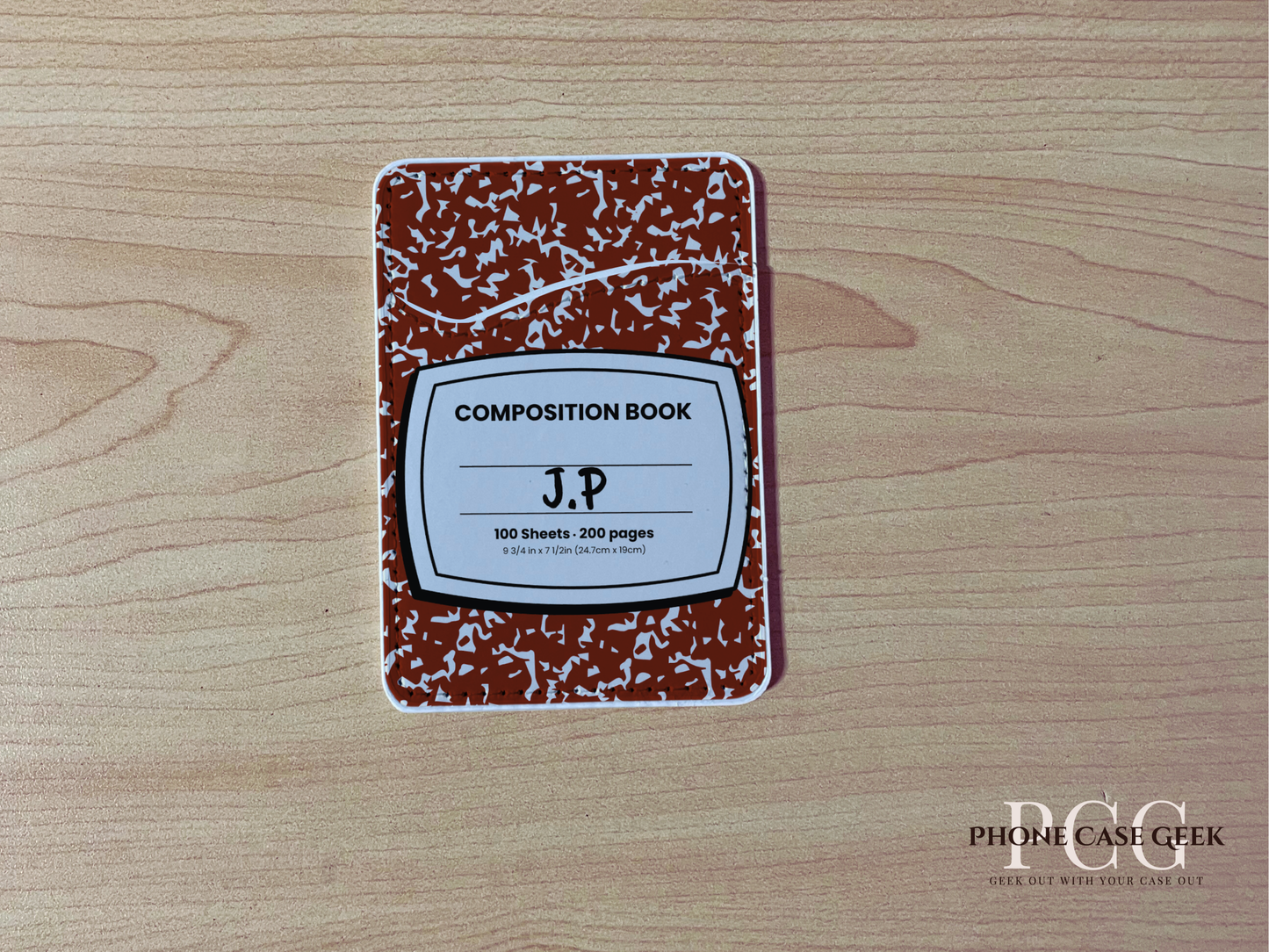 Custom adhesive phone wallet/card holder with red and white composition notebook design with surface "J.P" text on a wooden surface.