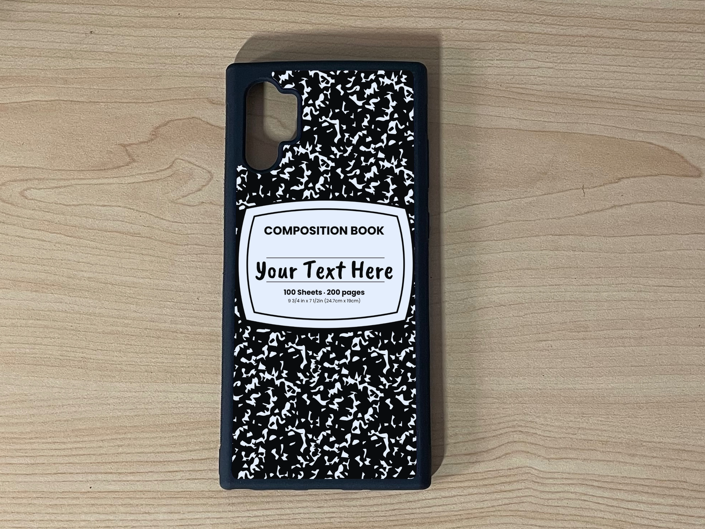 Custom phone case for the Samsung Note 10 Plus with a black and white composition notebook design with text "Your text here" on a wooden surface.