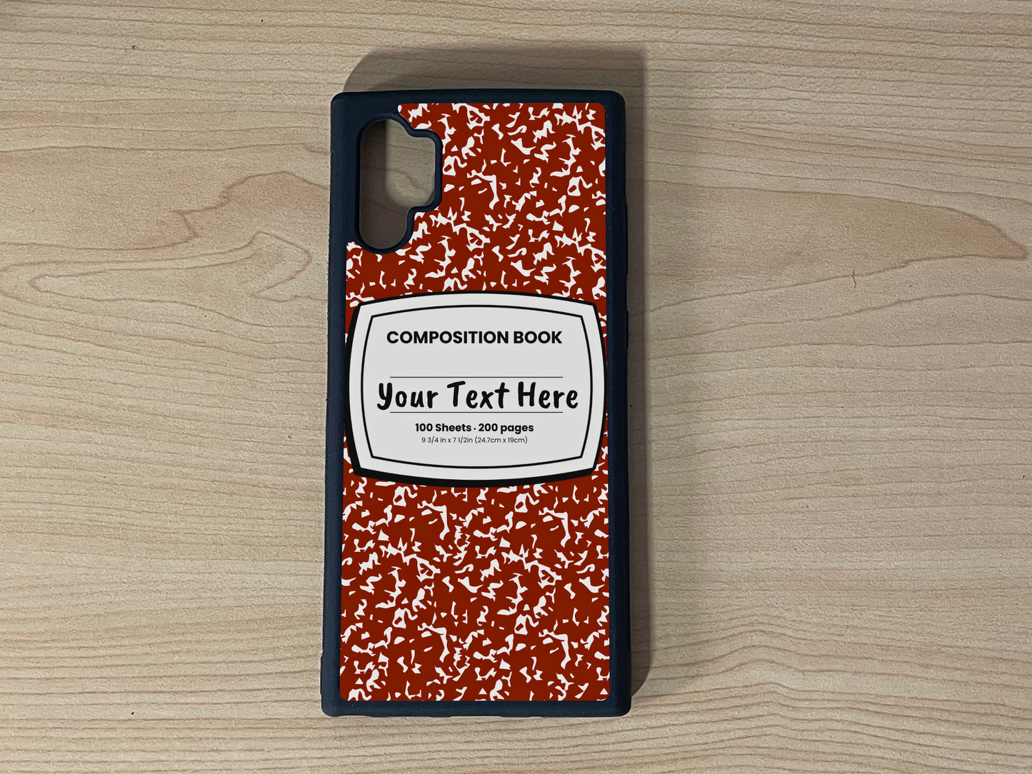 Custom phone case for the Samsung Note 10 Plus with a red and white composition notebook design with text "Your text here" on a wooden surface.