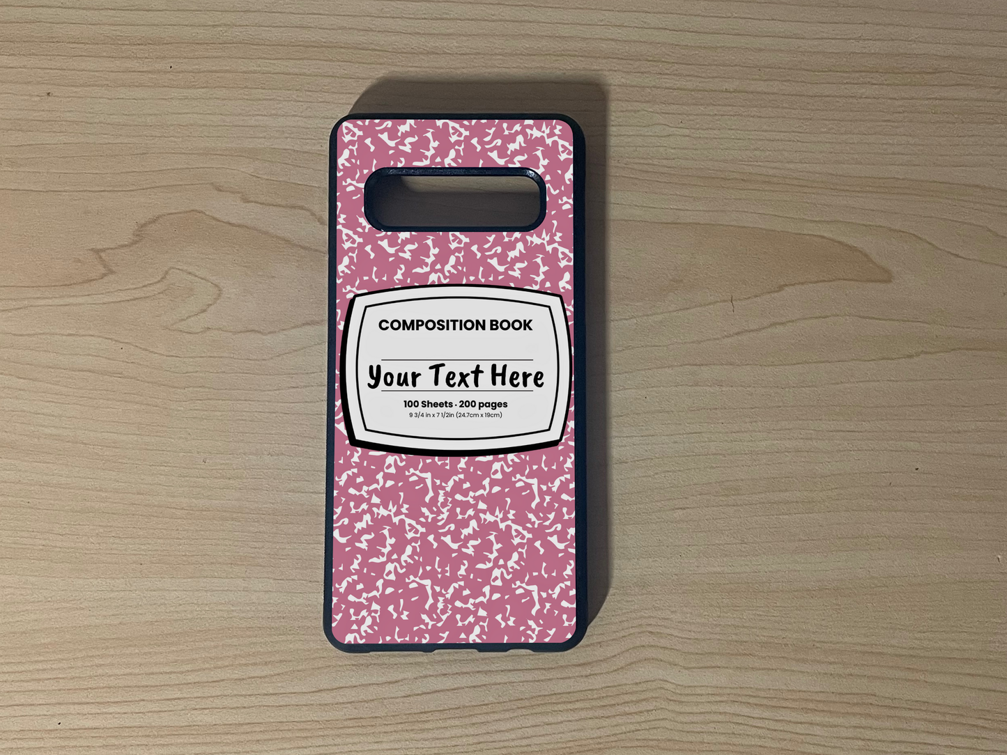 Custom phone case for the Samsung S10 and S10e with a pink and white composition notebook design with text "Your text here" on a wooden surface.