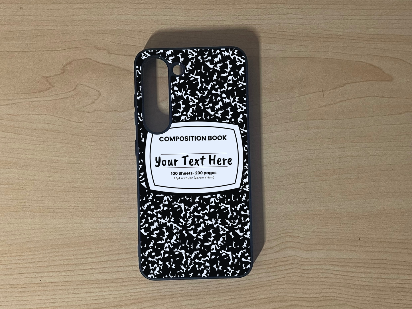 Custom phone case for the Samsung S23 and S23 Plus with a black and white composition notebook design with text "Your text here" on a wooden surface.