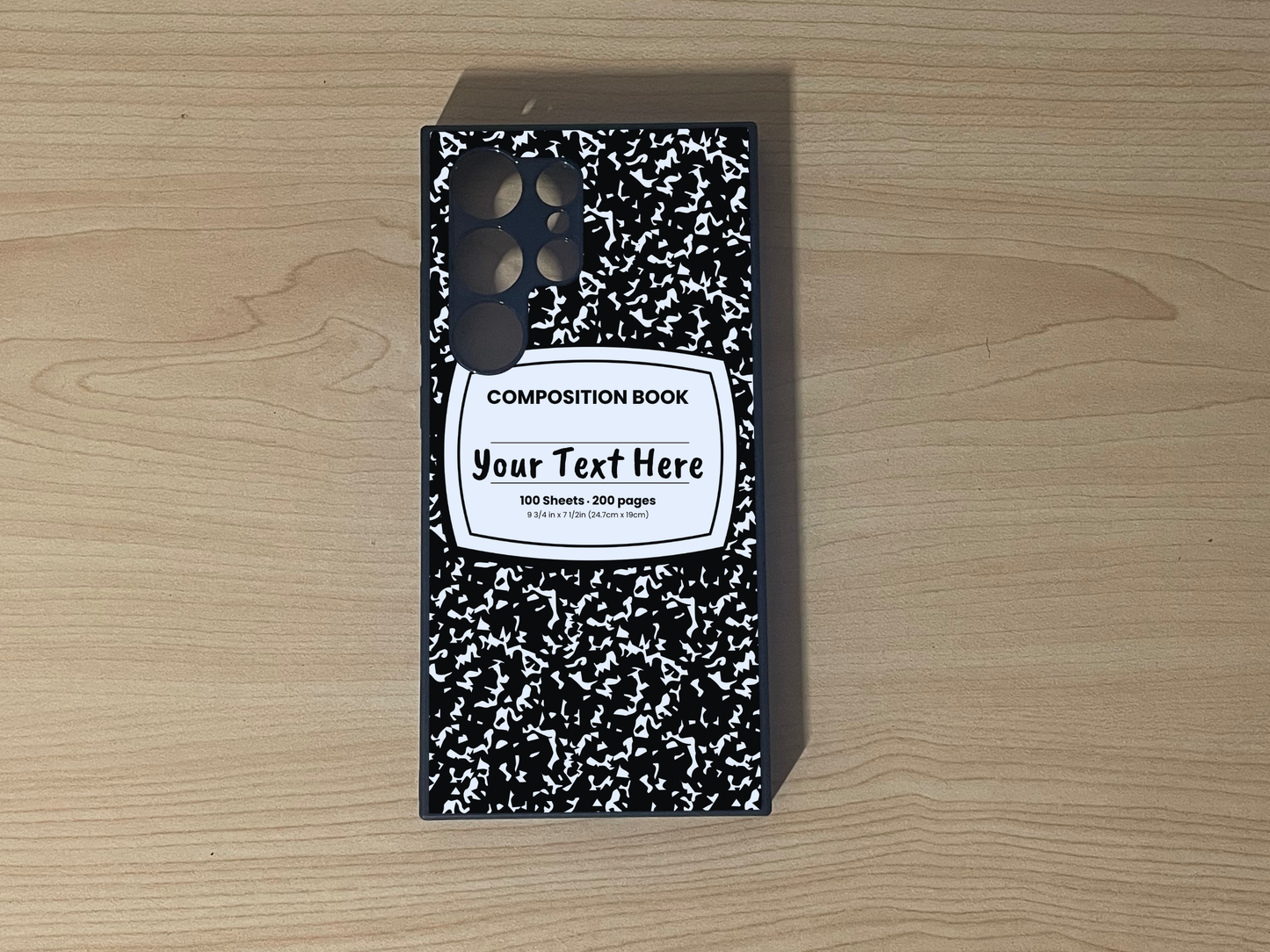 Custom phone case for the Samsung S24 Ultra, S23 Ultra, and S22. Ultra with a black and white composition notebook design with text "Your text here" on a wooden surface.