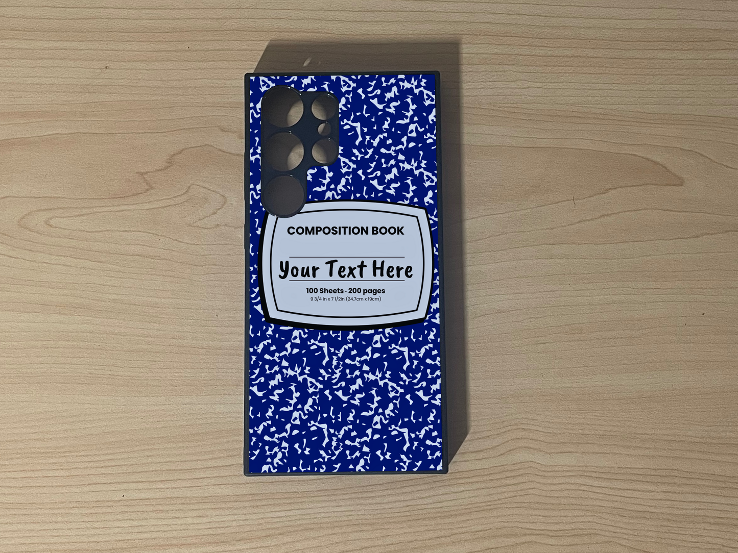 Custom phone case for the Samsung S24 Ultra, S23 Ultra, and S22 Ultra with a blue and white composition notebook design with text "Your text here" on a wooden surface.