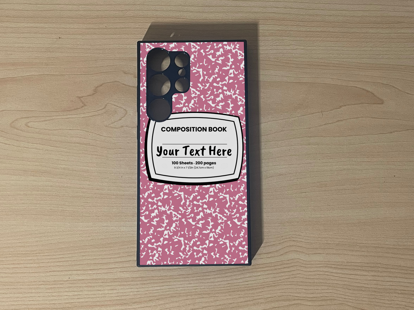 Custom phone case for the Samsung 24 Ultra, S23 Ultra and S22 Ultra with a pink and white composition notebook design with text "Your text here" on a wooden surface.