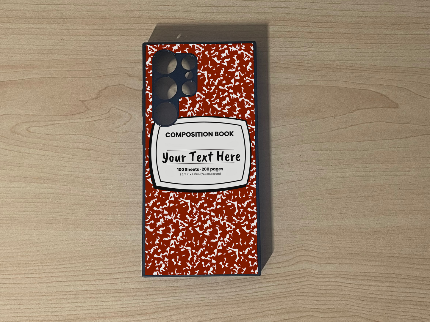 Custom phone case for the Samsung S24 Ultra, S23 Ultra and S22 Ultra with a red and white composition notebook design with text "Your text here" on a wooden surface.