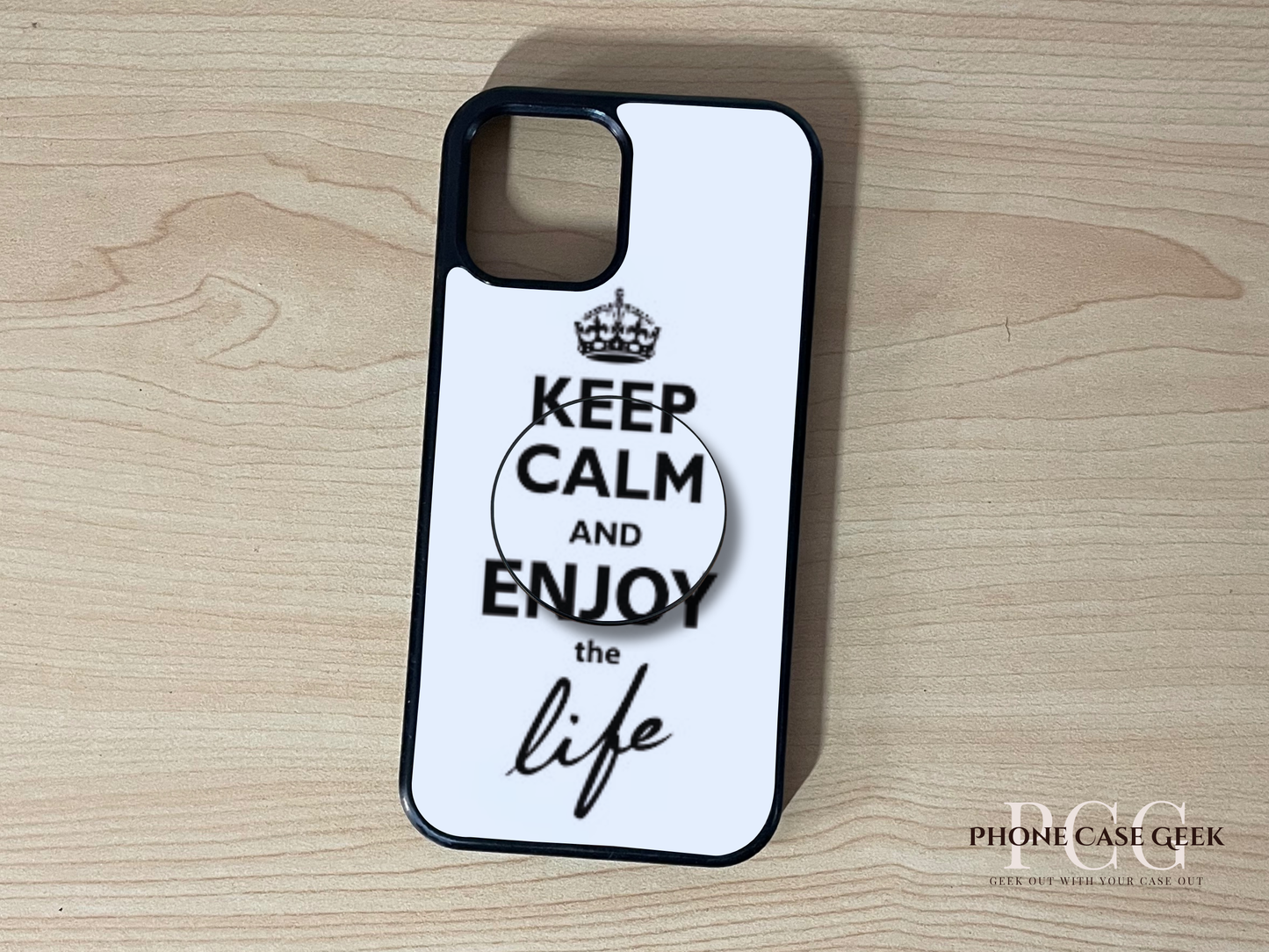 Custom iPhone case with 'Keep Calm and Enjoy the Life' text and matching adhesive phone grip on a wooden surface