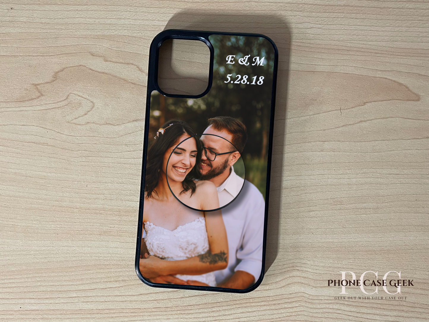 Custom iPhone case with photo of a couple and custom text initials on top with matching adhesive phone grip attached on a wooden surface.