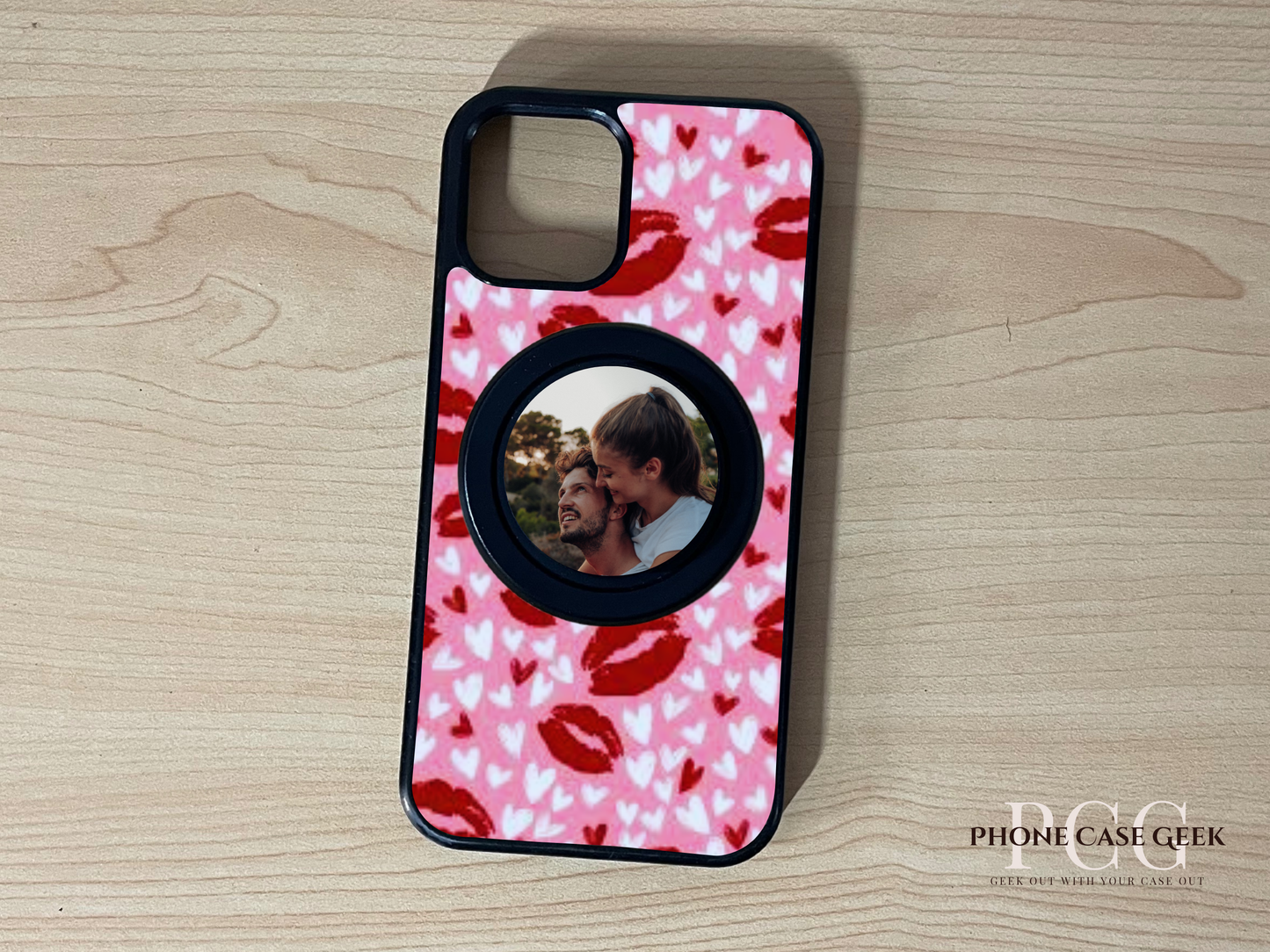 Custom Magsafe iPhone case with pink lip and heart pattern with custom black base Magsafe phone grip with a photo of a couple on a wooden surface