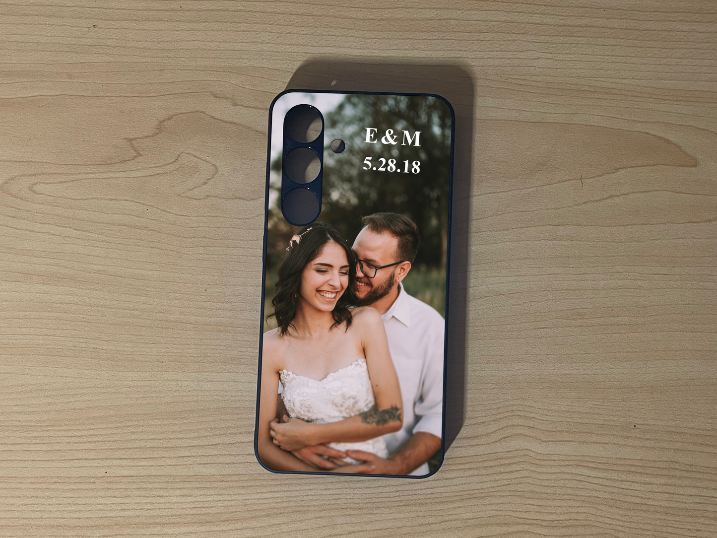 Custom phone case for the Samsung S24 and S24 Plus with a couple's photo and initials on a wooden surface.