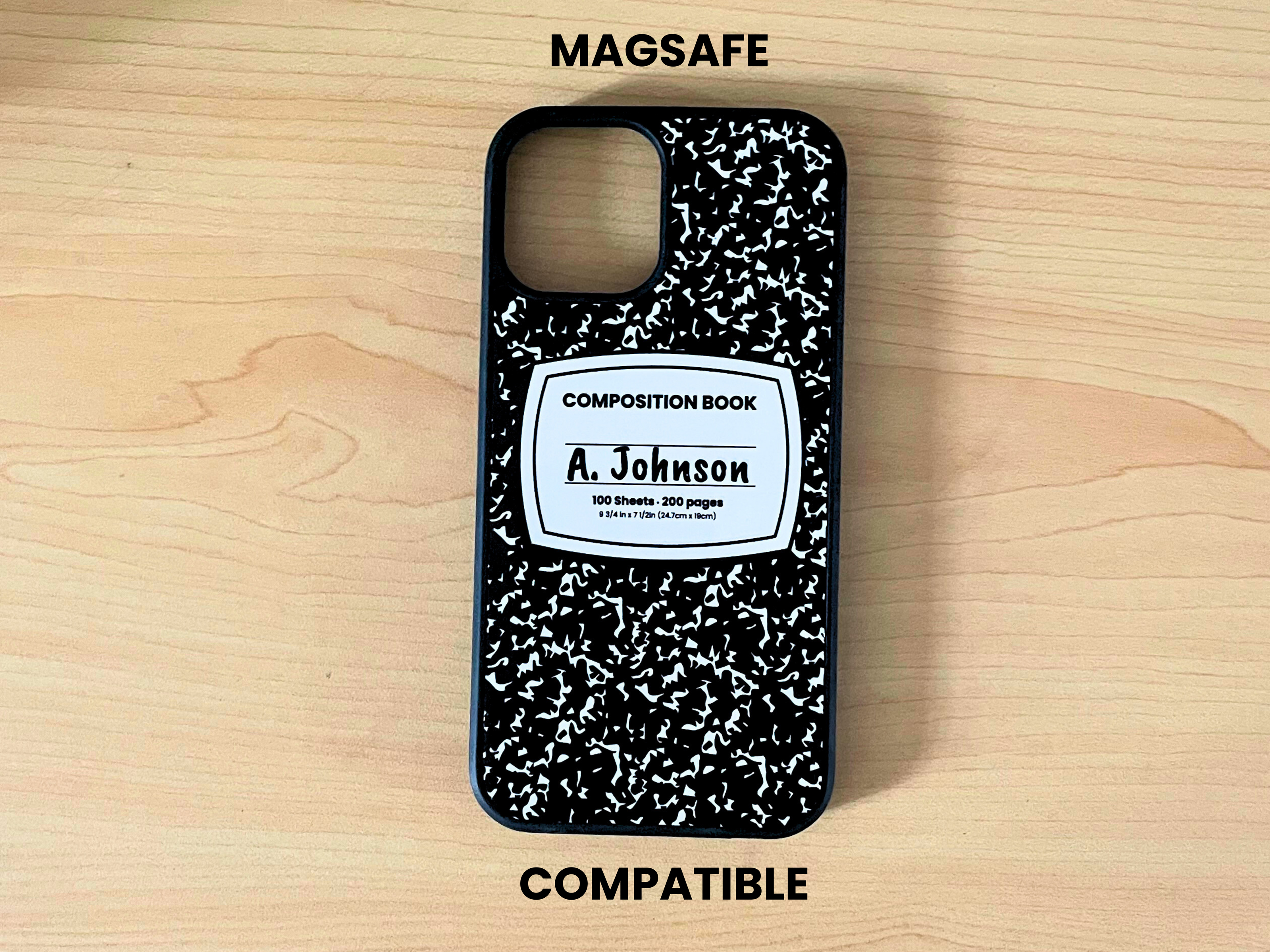 MagSafe iPhone case with black and white composition notebook design and 'A. Johnson' written in the middle displayed on a wooden surface.