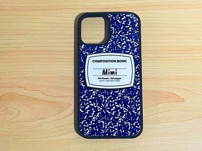 iPhone case with blue and white composition notebook design and 'Mimi' written in the middle displayed on a wooden surface.