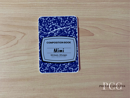 Custom phone wallet/card holder with blue and white composition notebook design with "Mimi" text on a wooden surface 