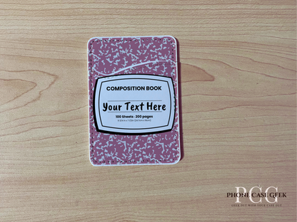 Custom adhesive phone wallet/card holder with pink and white composition notebook design on a wooden surface.