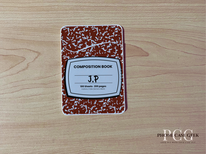 Custom adhesive phone wallet/card holder with red and white composition notebook design with surface "J.P" text on a wooden surface.