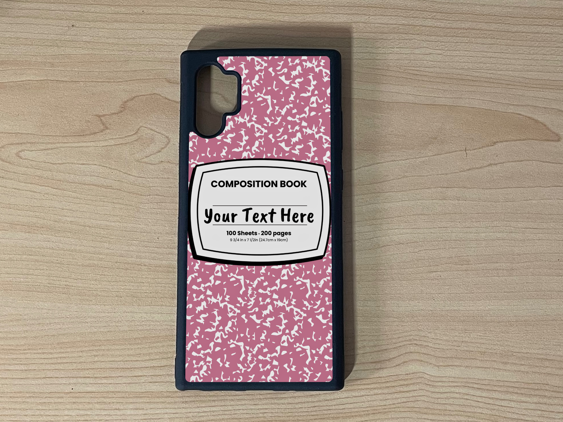 Custom phone case for the Samsung Note 10 Plus with a pink and white composition notebook design with text "Your text here" on a wooden surface.