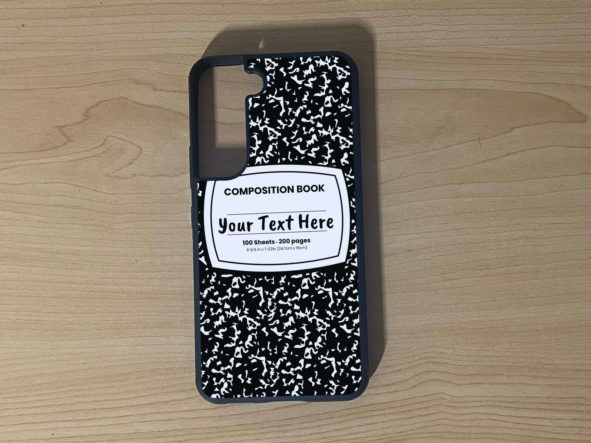 Custom phone case for the Samsung S21 and S21 Plus with a black and white composition notebook design with text "Your text here" on a wooden surface.