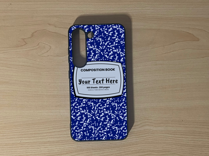 Custom phone case for the Samsung S23 and S23 Plus with a blue and white composition notebook design with text "Your text here" on a wooden surface.