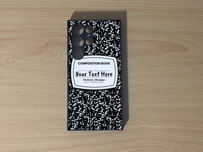 Custom phone case for the Samsung S24 Ultra, S23 Ultra, and S22. Ultra with a black and white composition notebook design with text "Your text here" on a wooden surface.