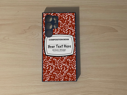 Custom phone case for the Samsung S24 Ultra, S23 Ultra and S22 Ultra with a red and white composition notebook design with text "Your text here" on a wooden surface.