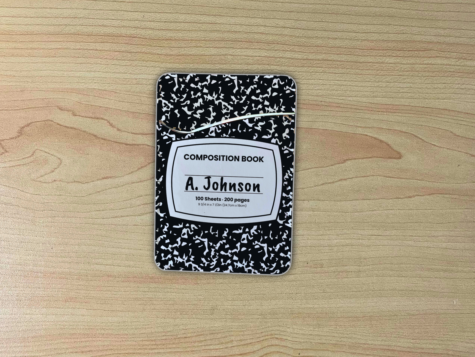 Black and white composition notebook adhesive phone wallet/card holder with custom text "A. Johnson" in the center on a wooden surface