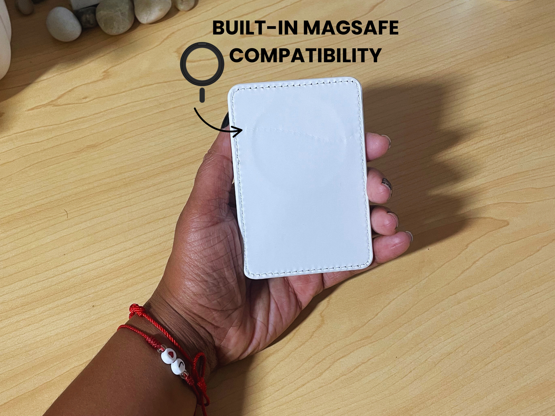 Hand holding a white phone card holder with showing the "BUILT-IN MAGSAFE COMPATIBILITY' text on a wooden surface.