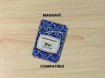 MagSafe compatible phone wallet/card holder with blue and white composition notebook design with customizable text "Mimi" on the center on a wood background.