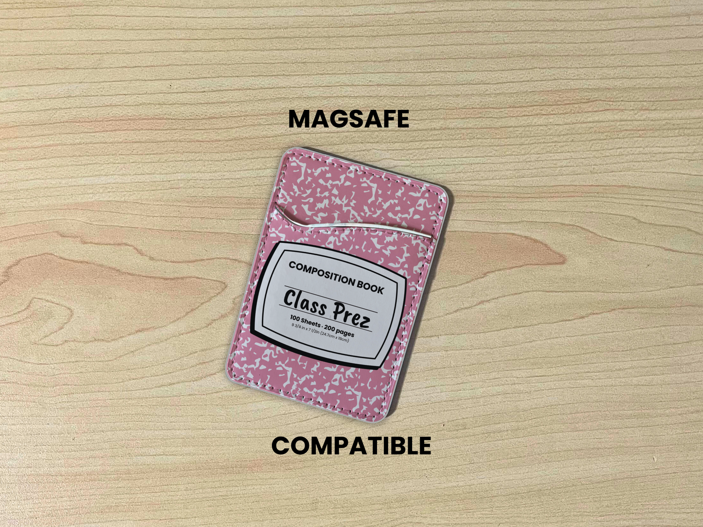 MagSafe compatible phone wallet/card holder with pink and white composition notebook design with customizable text "Class Prez" on the center on a wooden background.