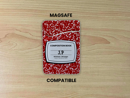 MagSafe compatible phone wallet/card holder with red and white composition notebook design with customizable text " J.P in the center on a wooden background.