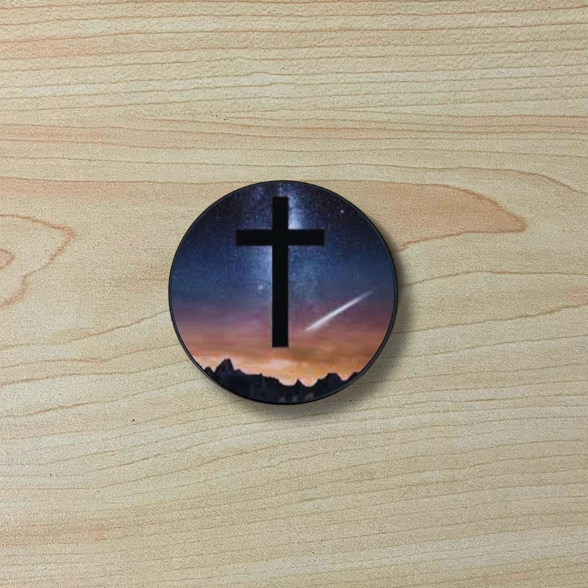 Custom adhesive phone grip with an image of a cross and the night sky on a wooden surface.