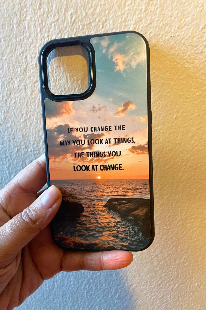 Custom phone case with sunset design and motivational quote held by a hand against a plain background