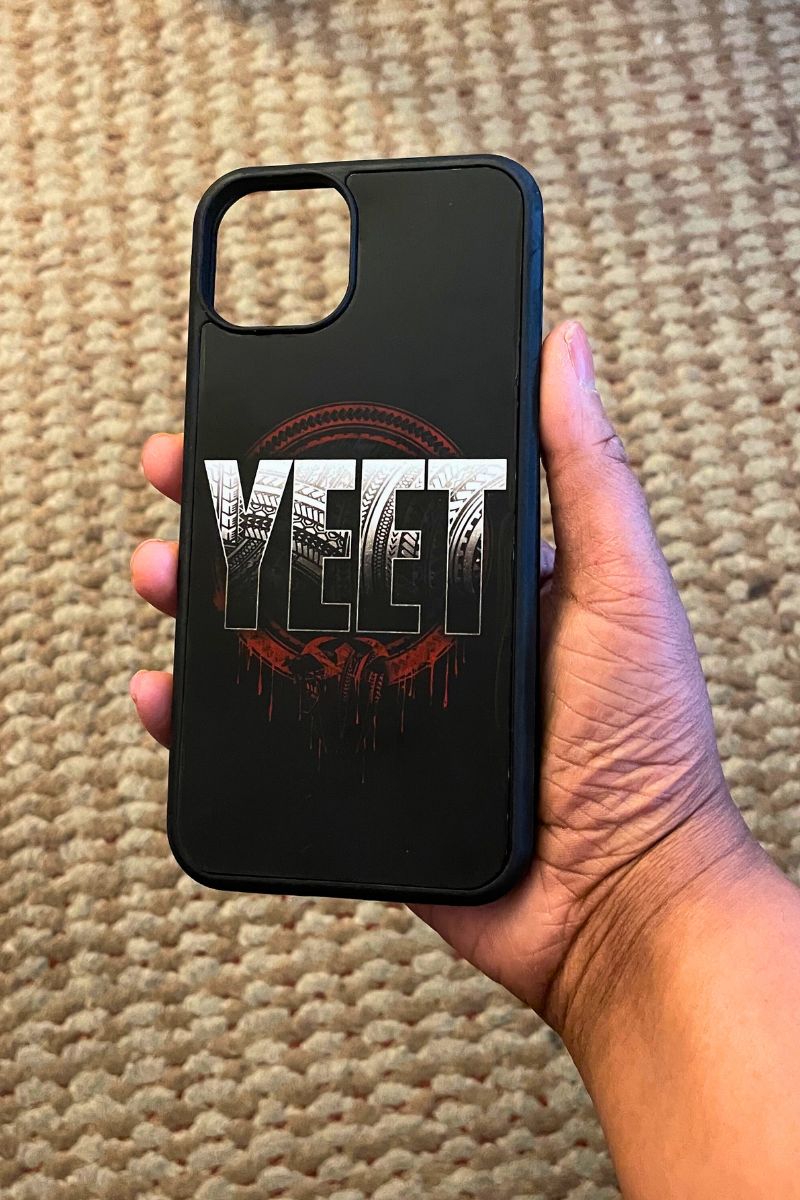 Custom phone case with 'YEET' design held by a hand on a textured surface