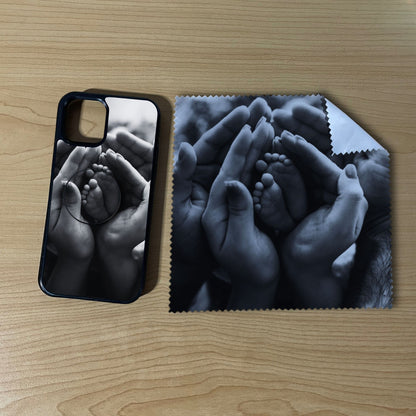 Custom iPhone case bundle set with hands holding a baby's foot design with matching phone grip and matching microfiber cloth phone screen cleaner on a wooden surface.