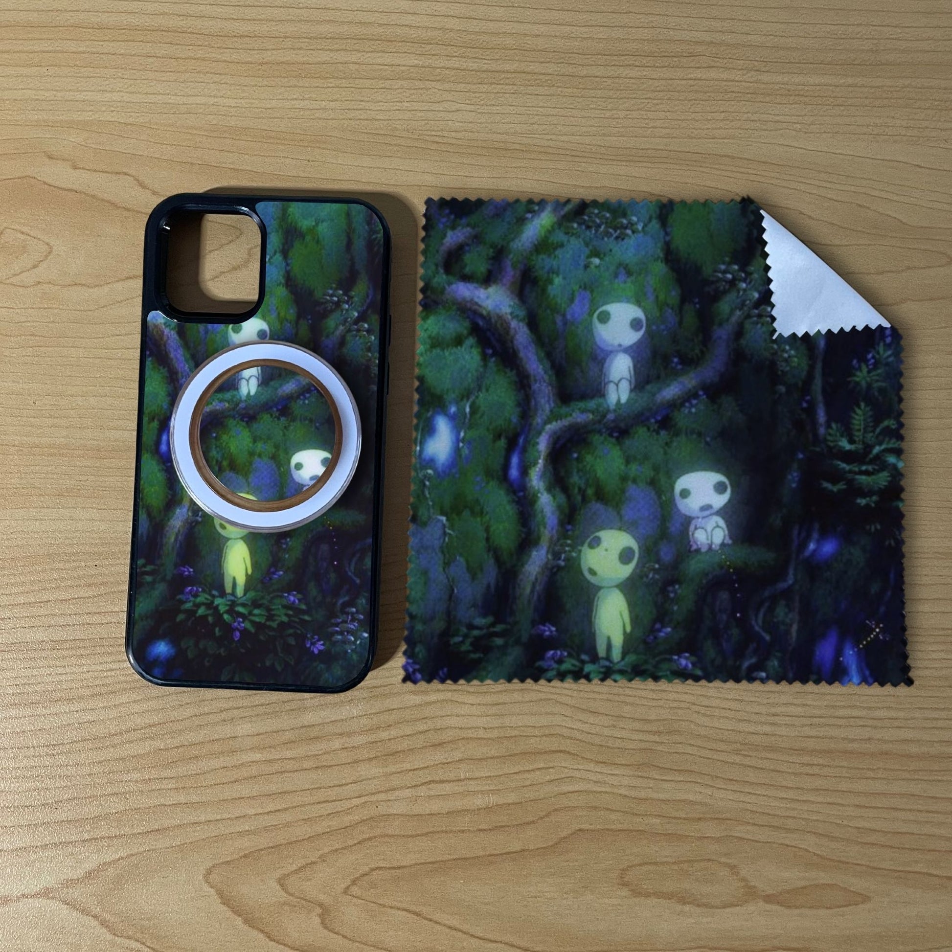 Custom MagSafe iPhone case bundle set with forest design with matching black phone grip and matching microfiber cloth phone screen cleaner on a wooden surface.