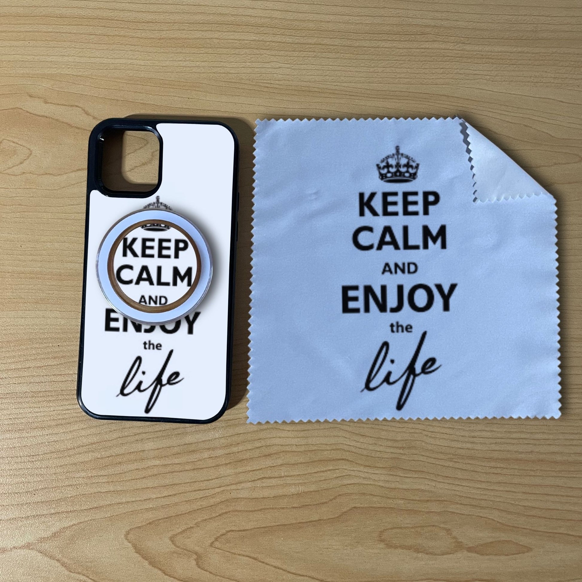 Custom MagSafe iPhone case bundle set with text "Keep calm and enjoy the life" design with matching clear phone grip and matching microfiber cloth phone screen cleaner on a wooden surface.