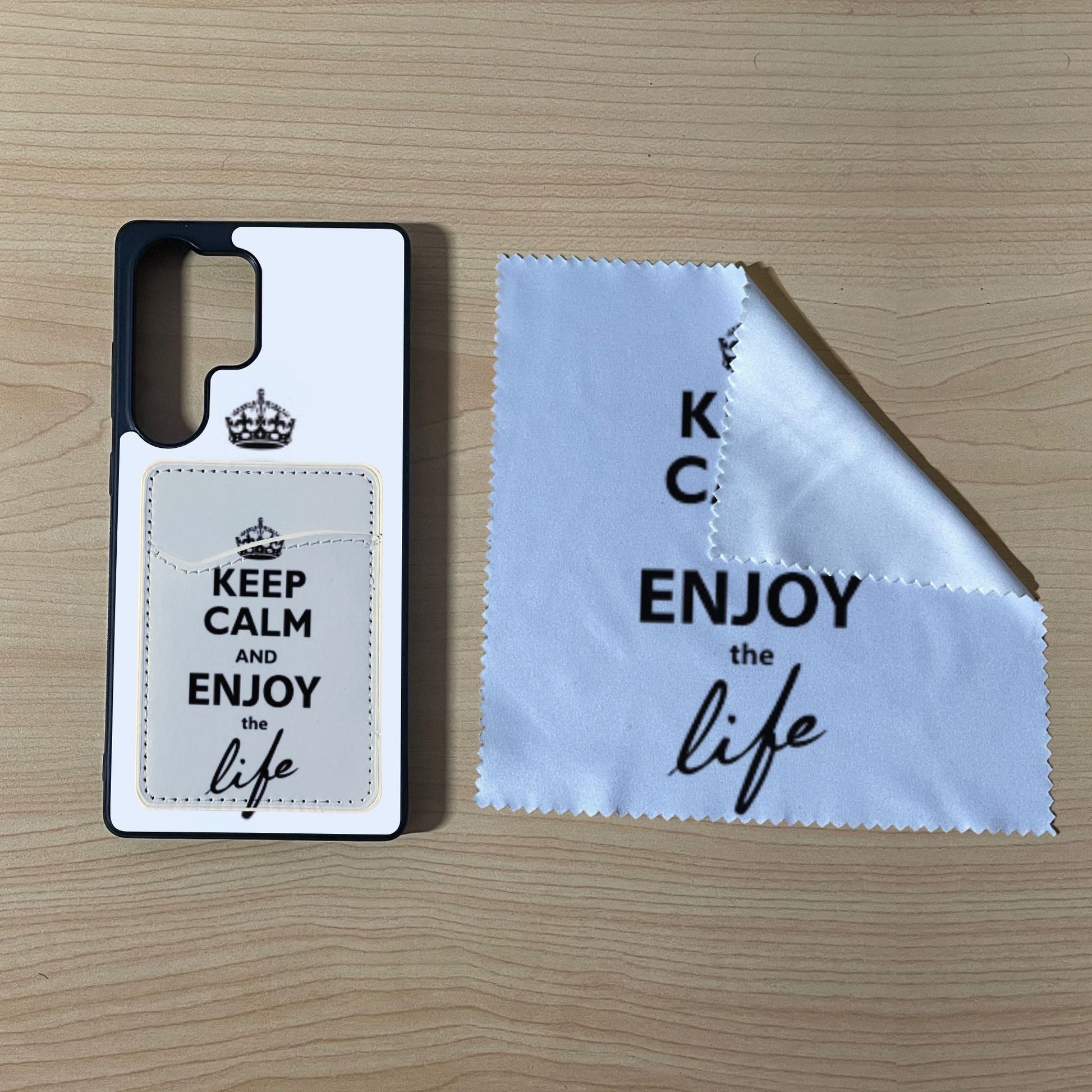 Custom Samsung S25 Ultra case with text "Keep calm and enjoy the life" with matching phone wallet card holder and matching microfiber cloth phone screen cleaner on a wooden surface