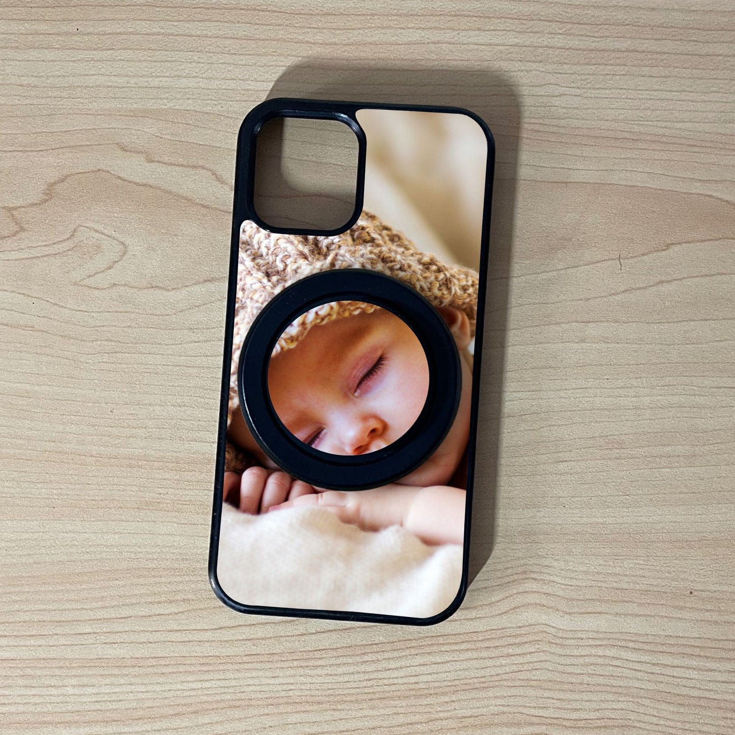 Custom iPhone case with a picture of a baby and matching magsafe phone grip on a wooden surface.