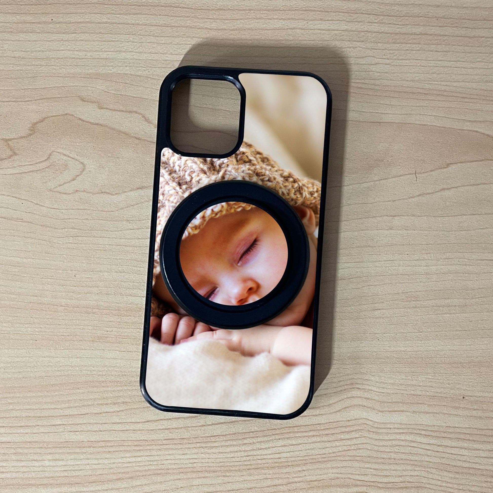 Custom iPhone case with a picture of a baby and matching magsafe phone grip on a wooden surface.
