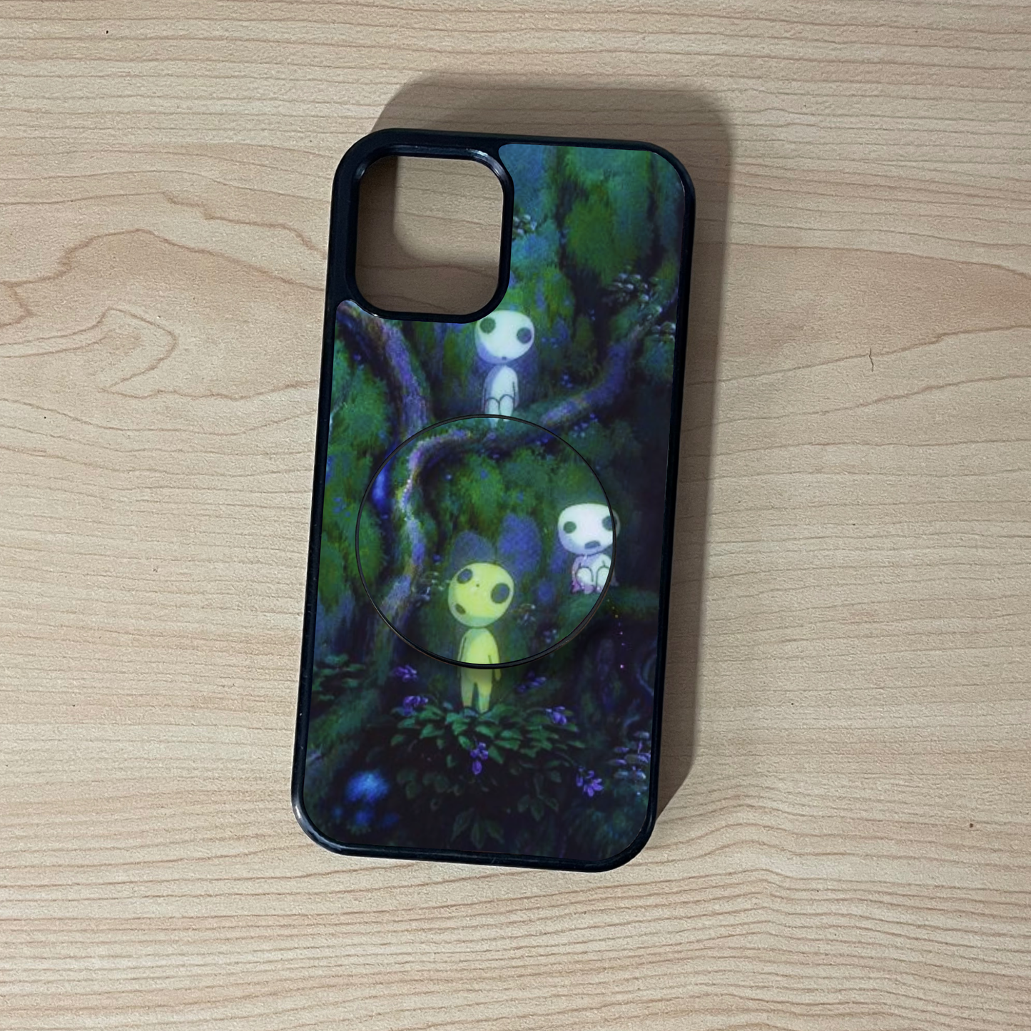 Custom iPhone case with a forest design and matching adhesive phone grip on a wooden surface
