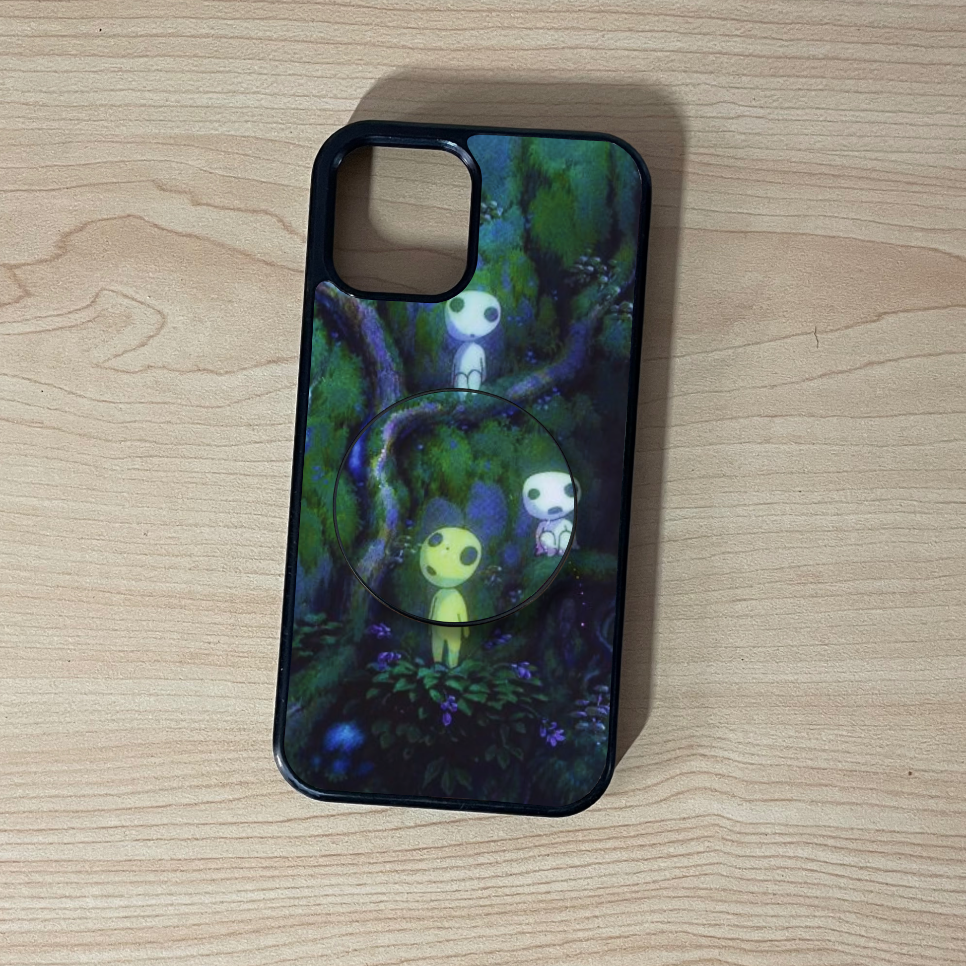 Custom iPhone case with a forest design and matching adhesive phone grip on a wooden surface