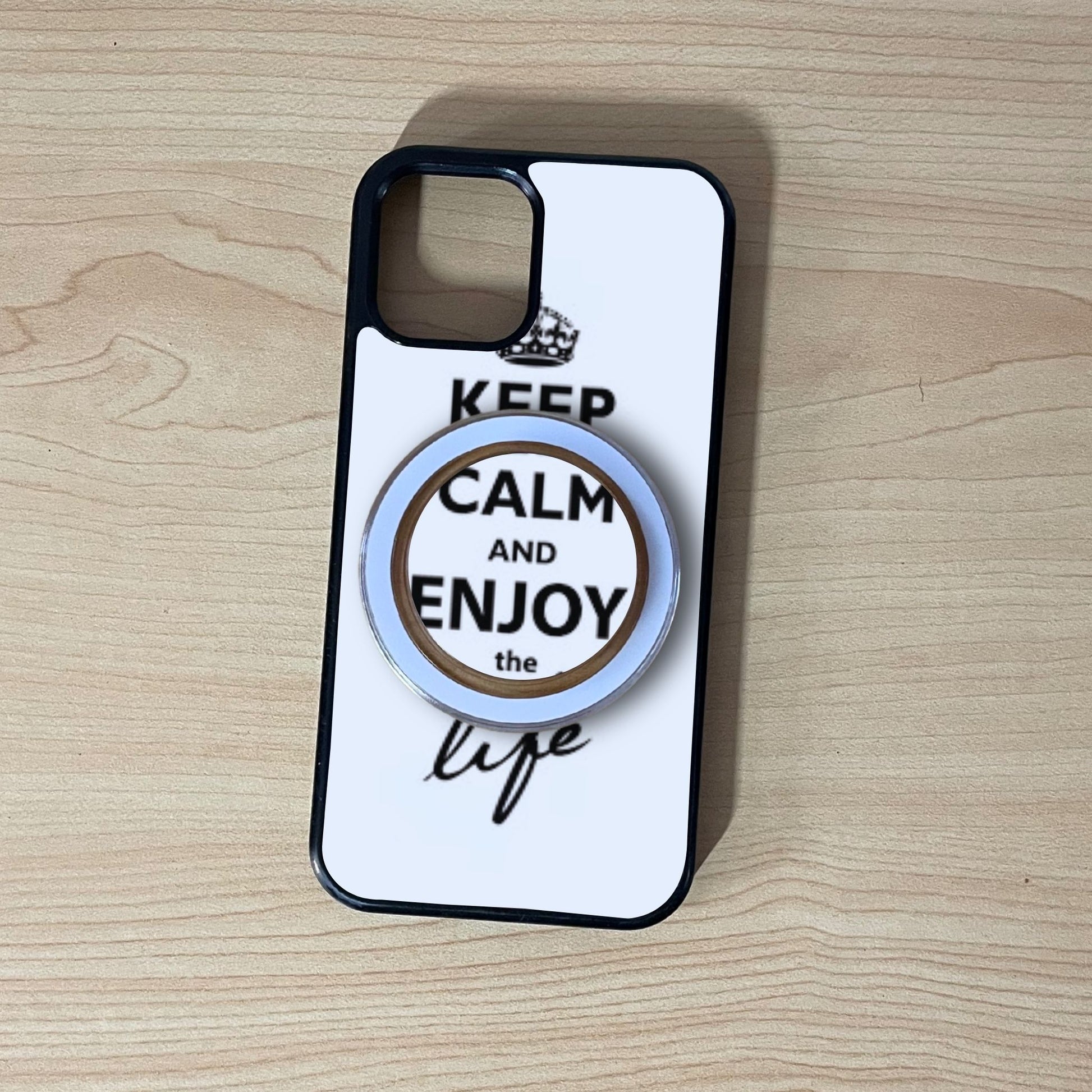 Custom iPhone case with 'Keep Calm and Enjoy the Life' text and matching magsafe clear phone grip on a wooden surface