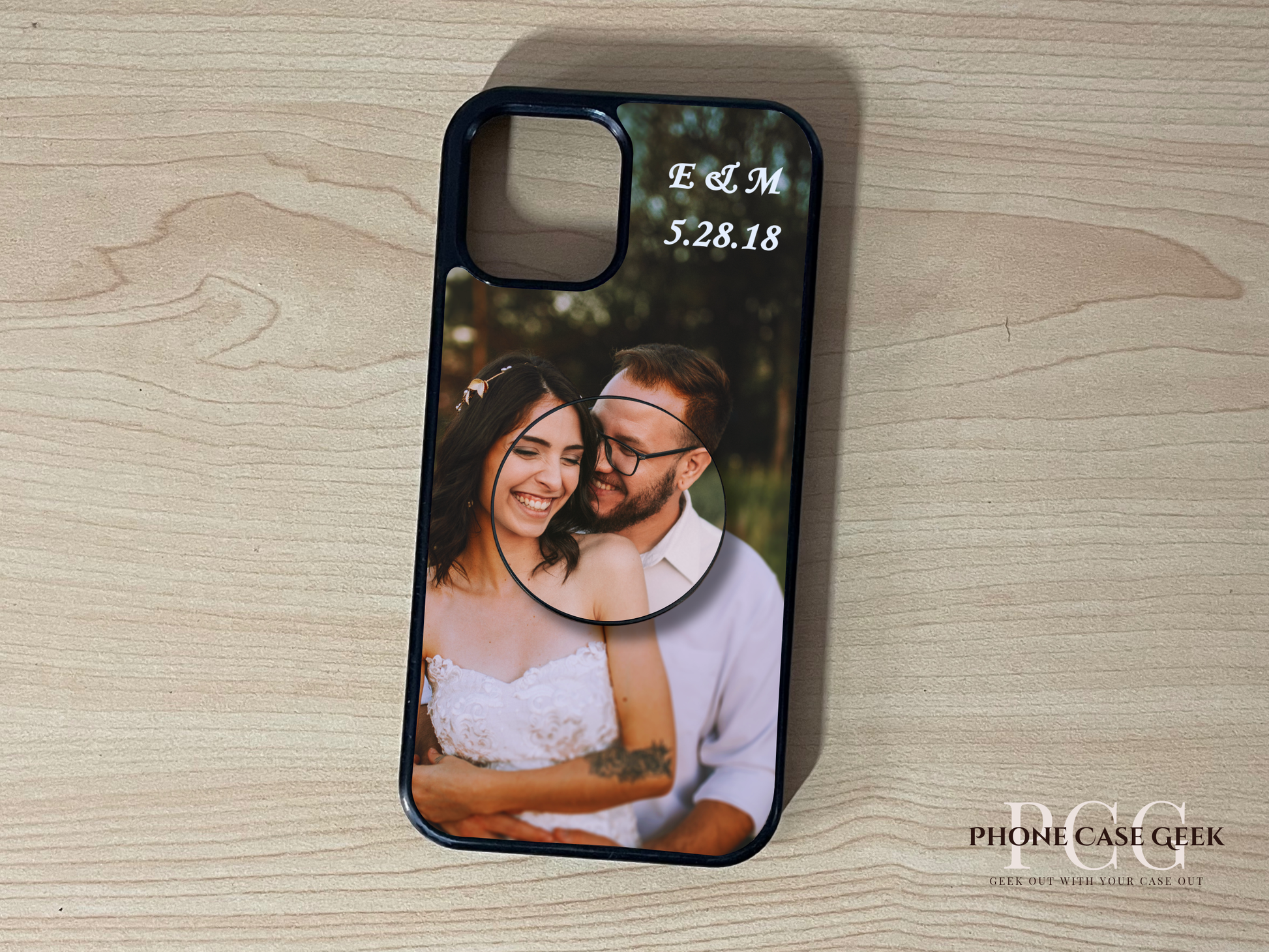 Custom iPhone case with photo of a couple and custom text initials on top with matching adhesive phone grip attached on a wooden surface. 