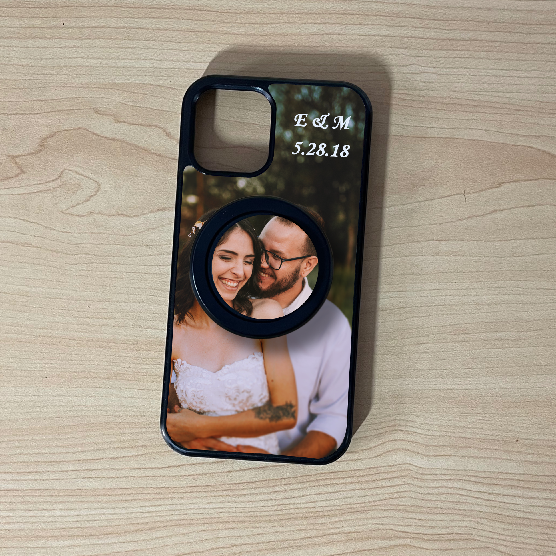Custom iPhone MagSafe case with photo of a couple and custom text initials on top with matching MagSafe phone grip attached on a wooden surface. 