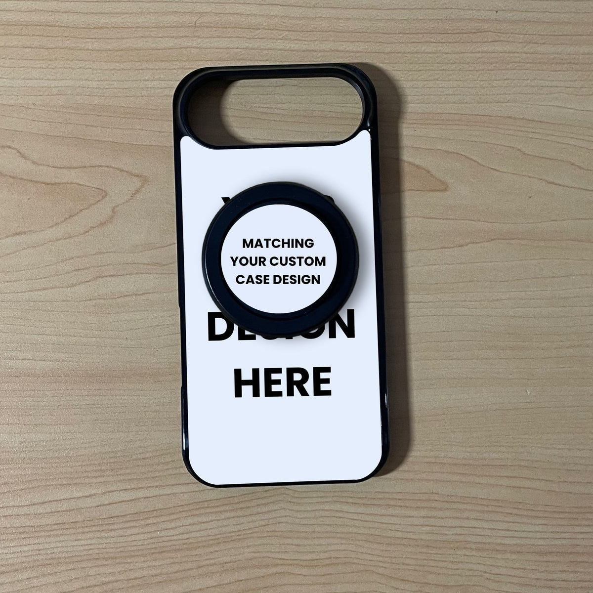 A MagSafe iPhone 17 Air customizable black phone case with a black MagSafe phone grip and placeholder text 'DESIGN HERE' on a light wood background.