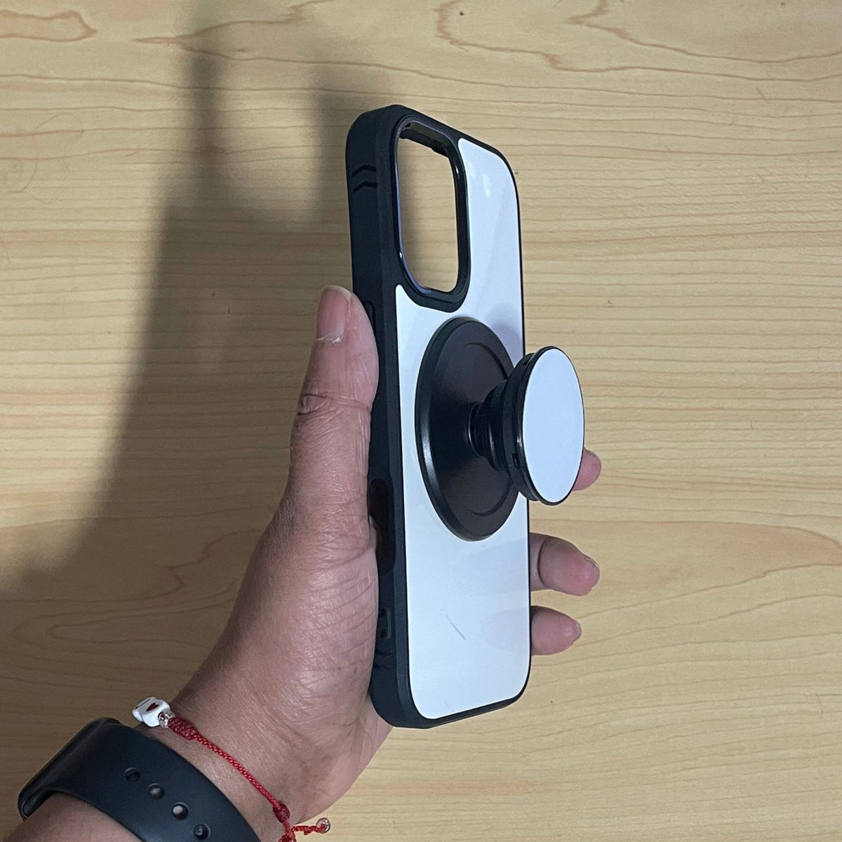 A hand holding a custom phone case with a built-in MagSafe PopSockets grip, set against a light wood grain background.