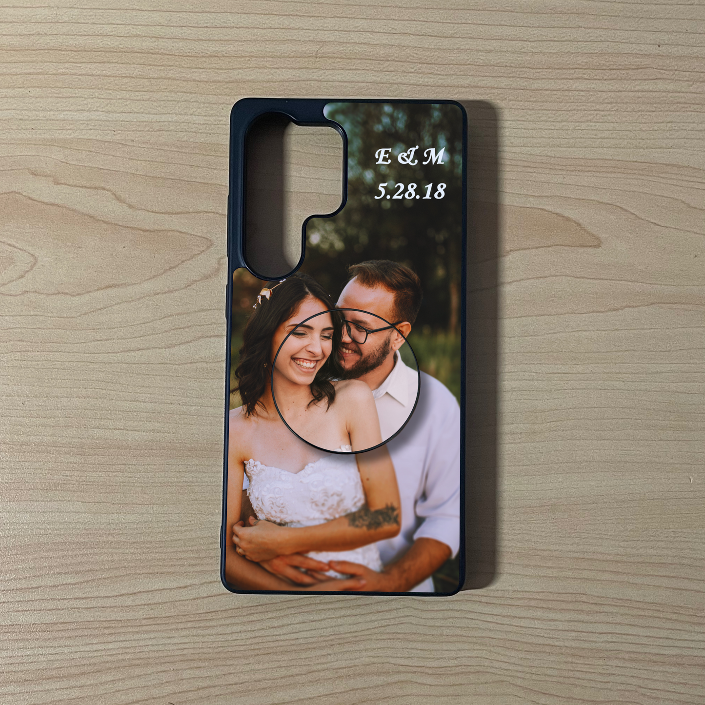 Samsung  S25 Ultra custom case with photo of a couple and custom text initials on top with matching adhesive phone grip attached on a wooden surface. 